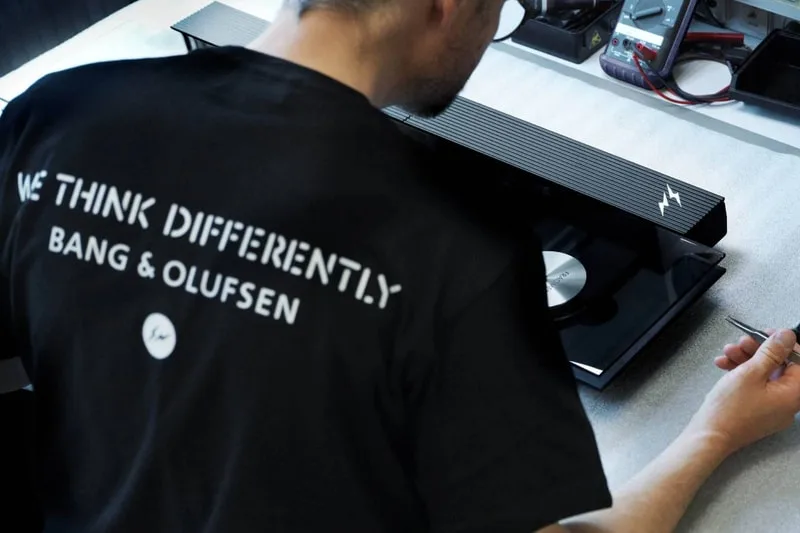 Homme travaillant sur un appareil Bang & Olufsen, texte "We Think Differently" visible.
