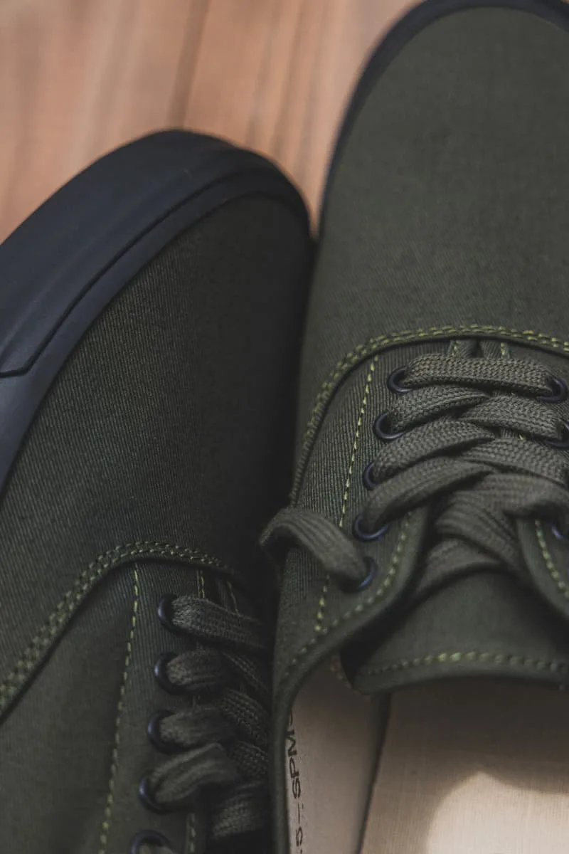 Chaussures en toile vert foncé avec semelle noire sur sol en bois.