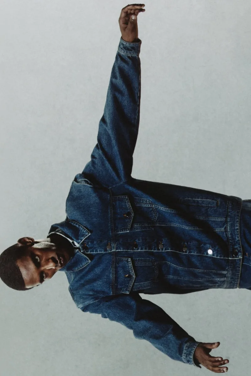 Homme en veste en jean posant contre un fond gris.