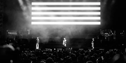 Concert en noir et blanc avec trois artistes sur scène devant le public.