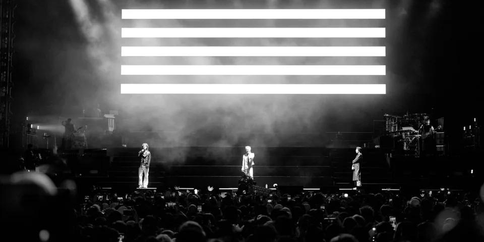 Concert en noir et blanc avec trois artistes sur scène devant le public.