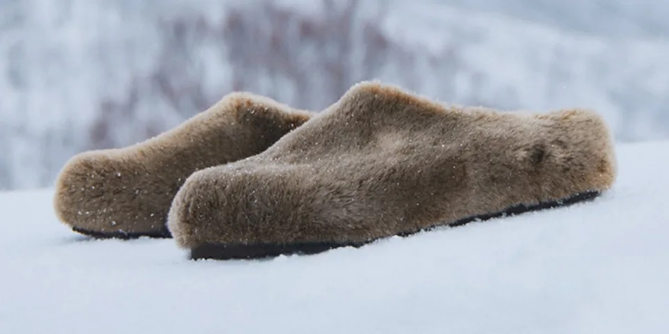 Pantoufles en fausse fourrure beige sur de la neige.