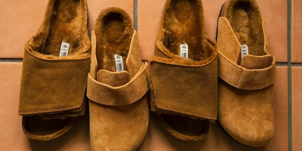 Quatre chaussons en daim marron doublés de fourrure, posés sur un carrelage