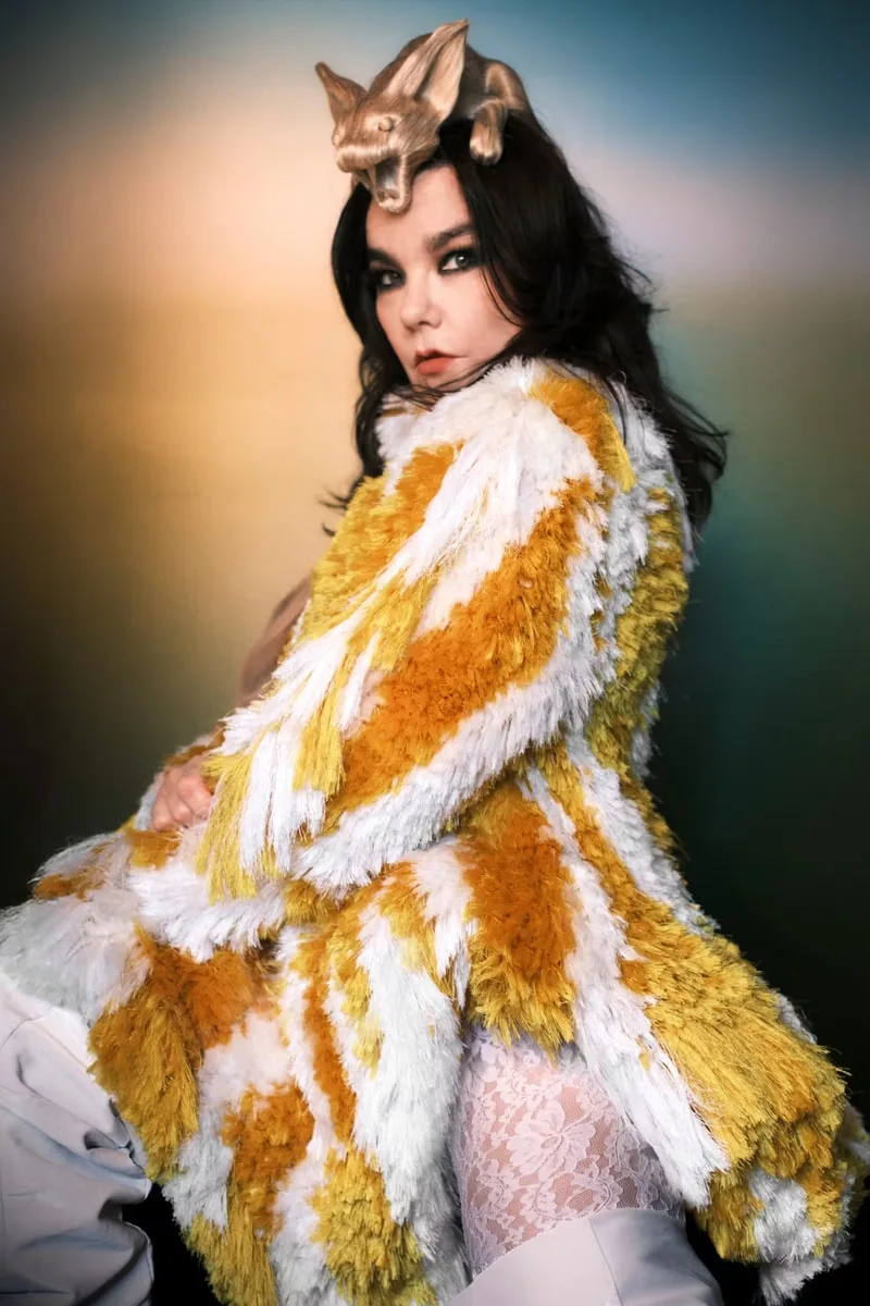 Personne en manteau jaune et blanc, accessoire tête unique, fond flou.