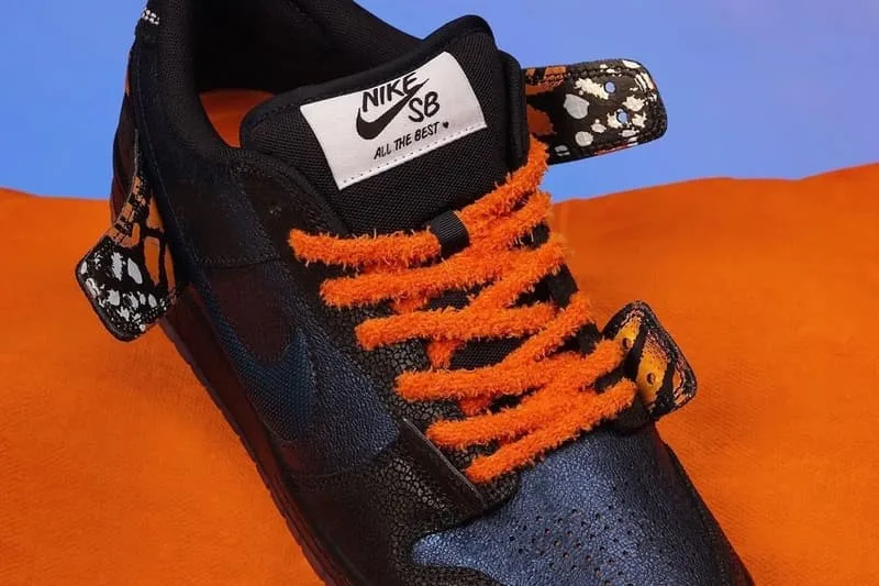 Chaussure Nike SB noir et orange avec motif de papillon, fond orange.