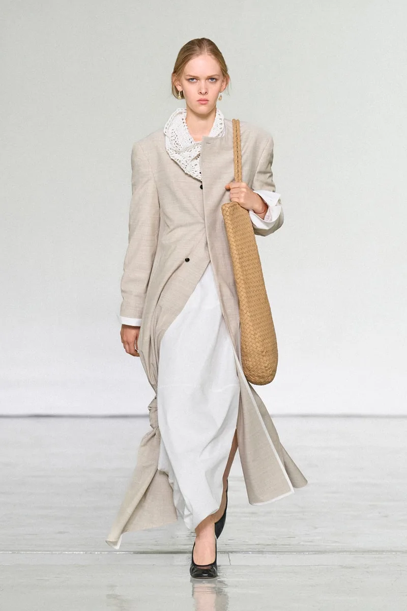 Défilé avec modèle en manteau beige et sac en osier.