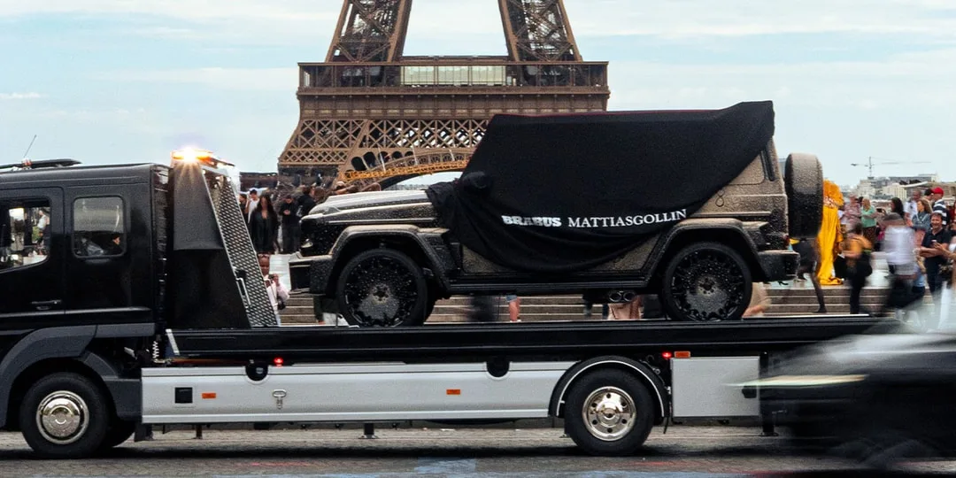 Voiture couverte sur un camion-plateau devant la tour Eiffel, foule en arrière-plan.