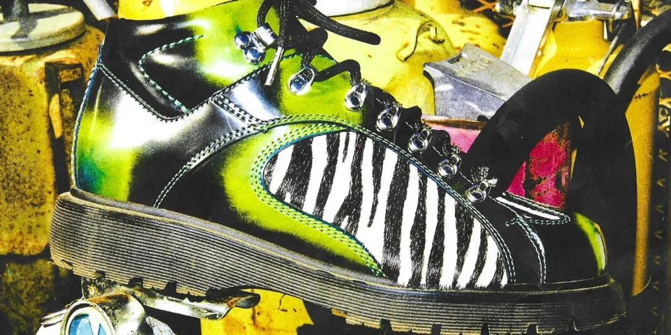 Bottine noire et vert fluo à motif zébré, posée parmi des objets colorés.