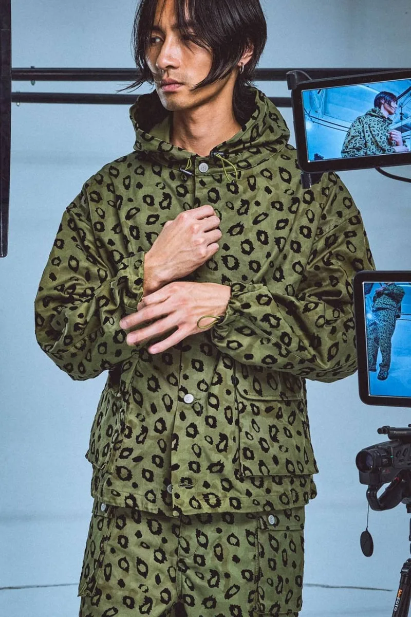 Homme portant une veste à motif léopard vert, avec des appareils photo autour.