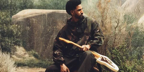 Homme assis avec guitare et fond naturel artistique.