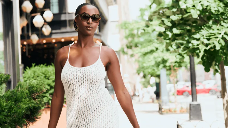 Femme élégante en robe blanche à l'extérieur, portant des lunettes de soleil.