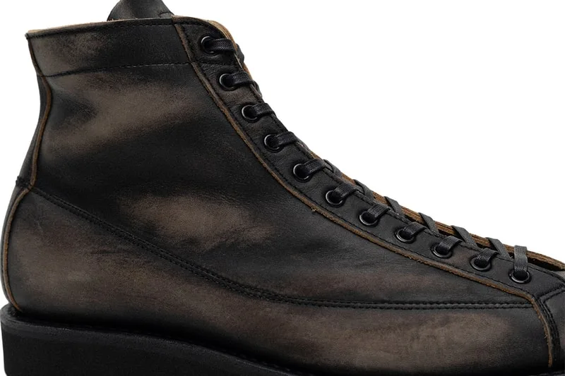 Chaussure en cuir foncé à lacets noirs, style moderne et usé.