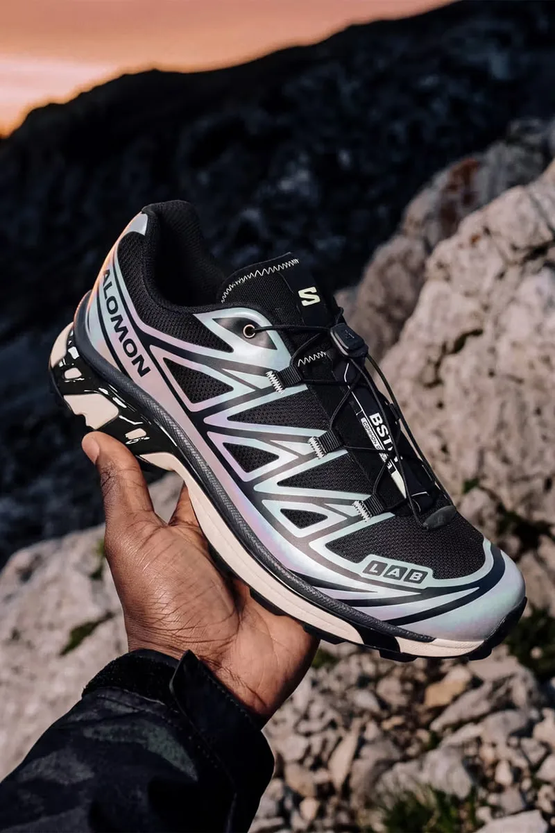 Homme tenant une chaussure de sport Salomon sur un terrain rocheux.