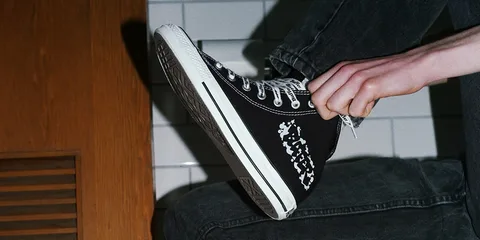Personne portant des baskets noires avec motif blanc, sur fond de carrelage.
