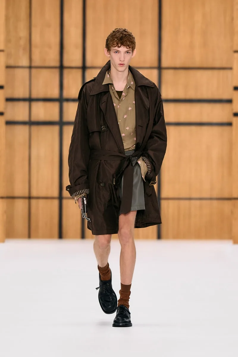 Homme défilant en trench-coat marron et chemise imprimée.