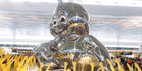 Grande sculpture argentée avec des figures jaunes et une foule environnante