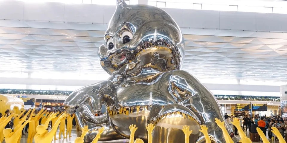 Grande sculpture argentée avec des figures jaunes et une foule environnante