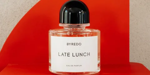 Flacon de parfum Byredo intitulé 'Late Lunch' sur fond rouge.