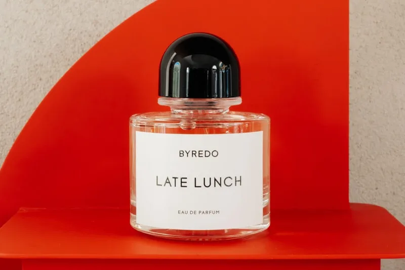 Flacon de parfum Byredo nommé Late Lunch sur fond rouge.