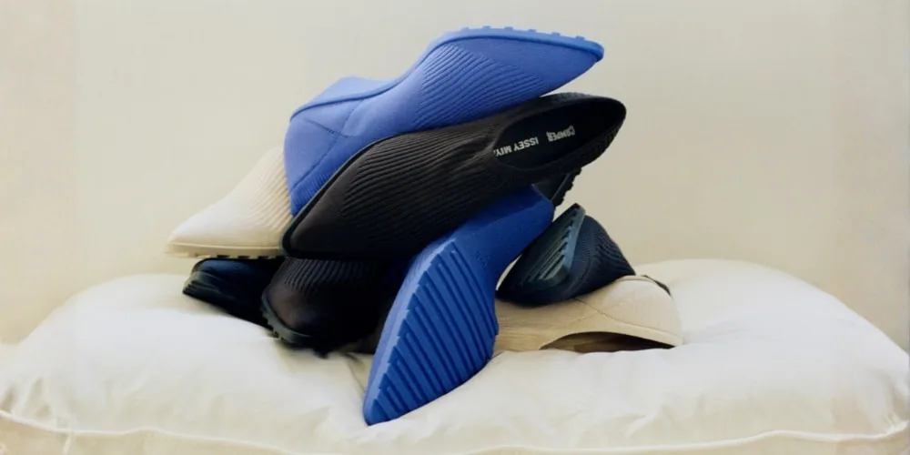 Pile de chaussures colorées, principalement bleu et beige, sur un coussin blanc.
