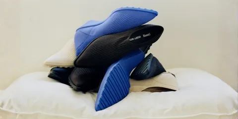 Pile de chaussures colorées, principalement bleu et beige, sur un coussin blanc.