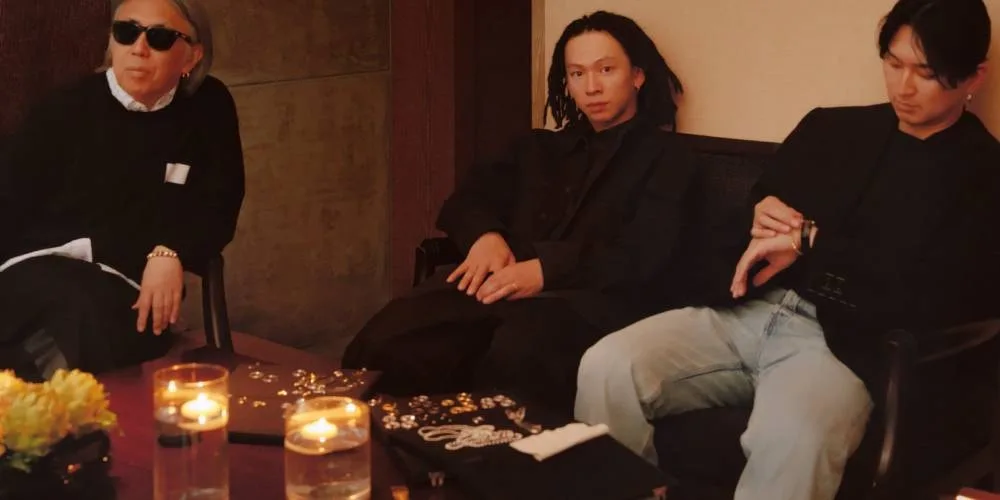 Trois hommes assis, bougies et fleurs sur la table, ambiance décontractée.