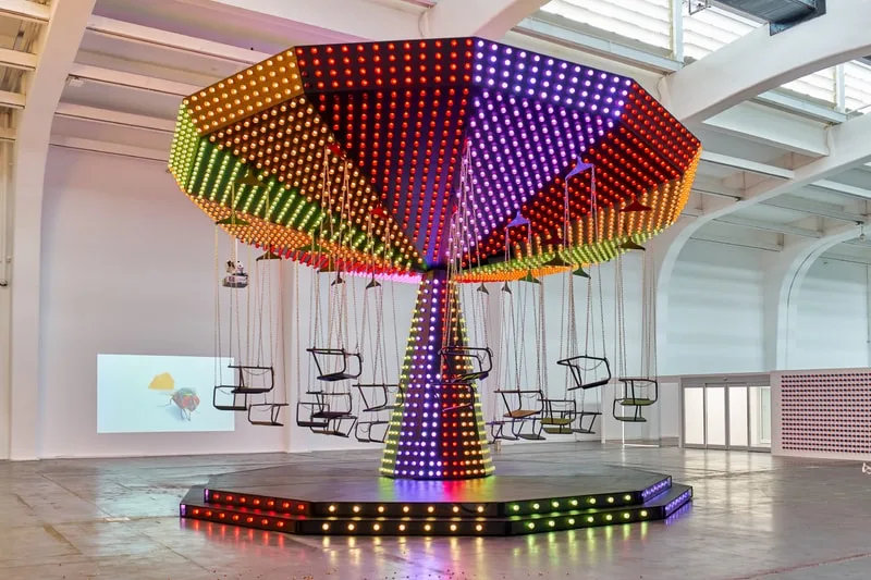 Carrousel lumineux moderne avec des sièges suspendus dans une salle vaste.