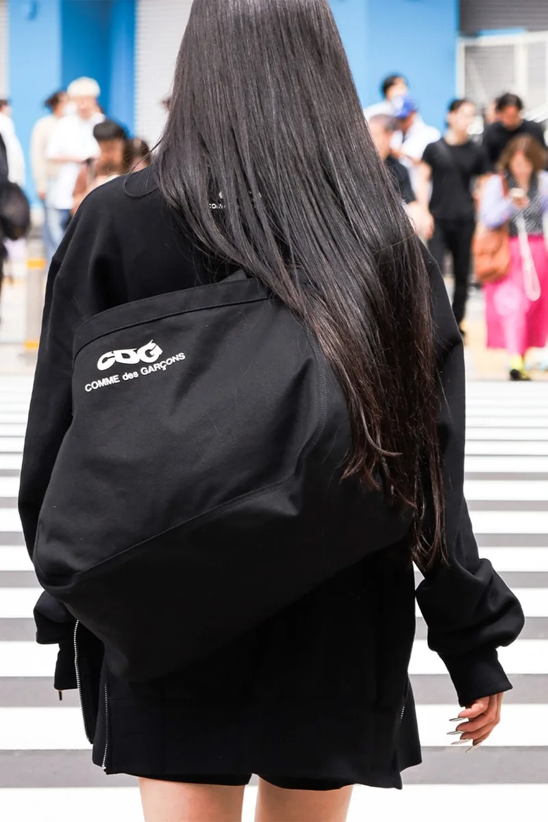 Personne portant un sac avec texte "Comme des Garçons" sur passage piéton.