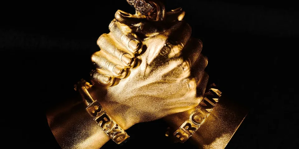 Deux mains dorées se serrant, bracelets 'BRVXX' visibles.