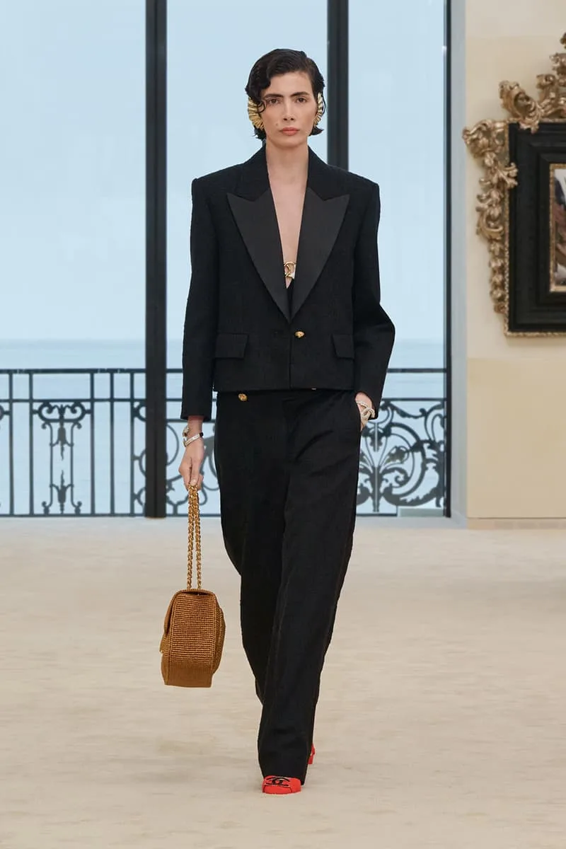 Femme en tailleur noir élégant, sac marron, intérieur luxueux.