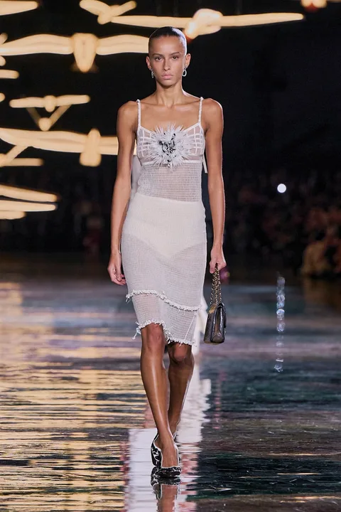 Modèle défilant en robe sur podium brillant avec éclairage artistique.