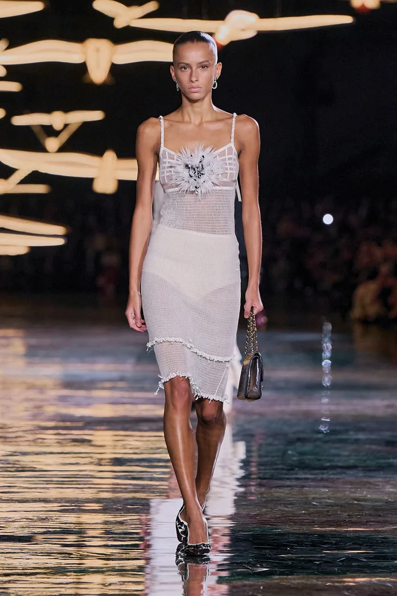 Modèle défilant en robe sur podium brillant avec éclairage artistique.