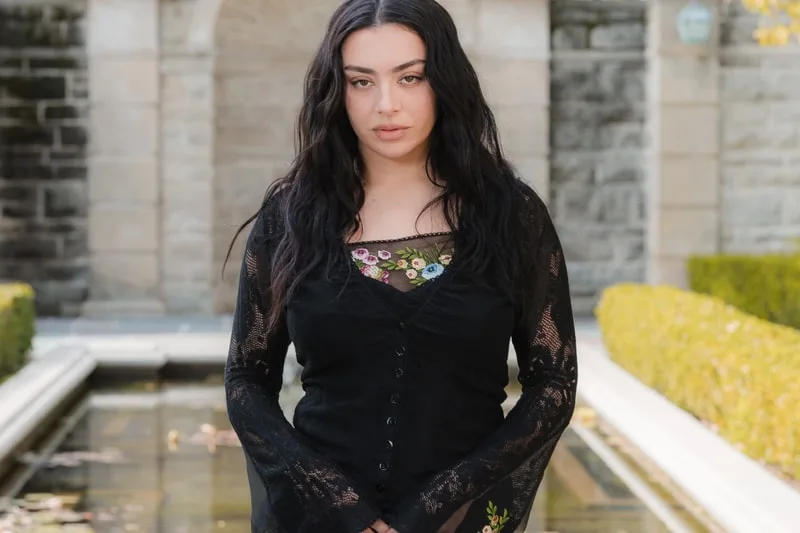 Femme en noir devant une fontaine et des buissons.
