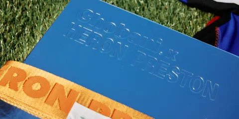 Étiquette bleue avec texte Chobani x Heron Preston sur herbe.