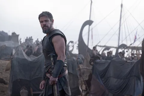 Guerrier en armure devant des bateaux vikings sur une plage.