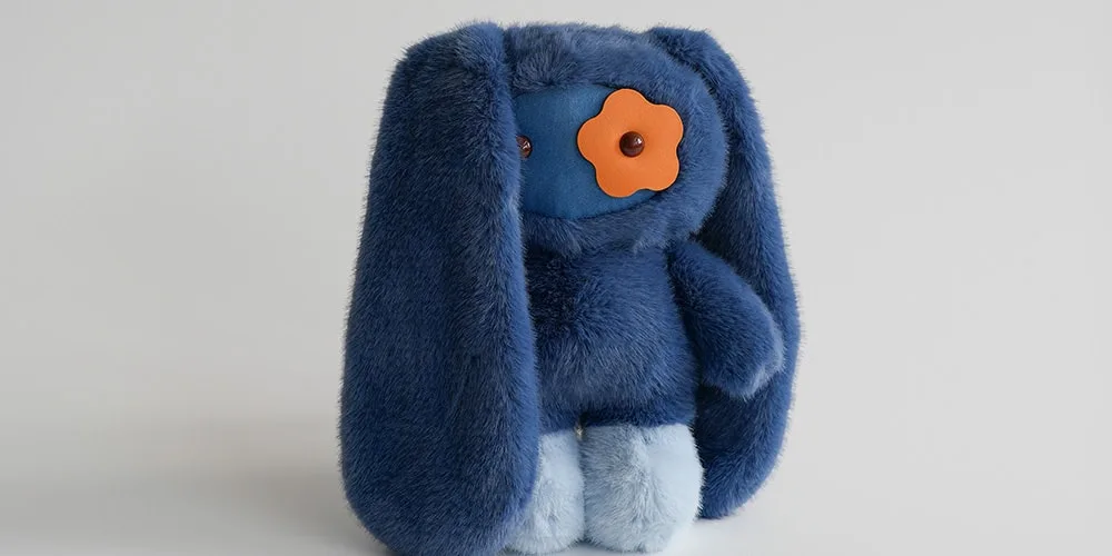 Peluche bleue avec de longues oreilles et une fleur orange sur le visage.