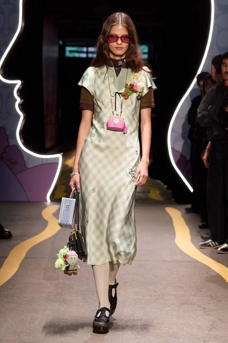 Défilé mode femme en robe verte, lunettes soleil et accessoires colorés.