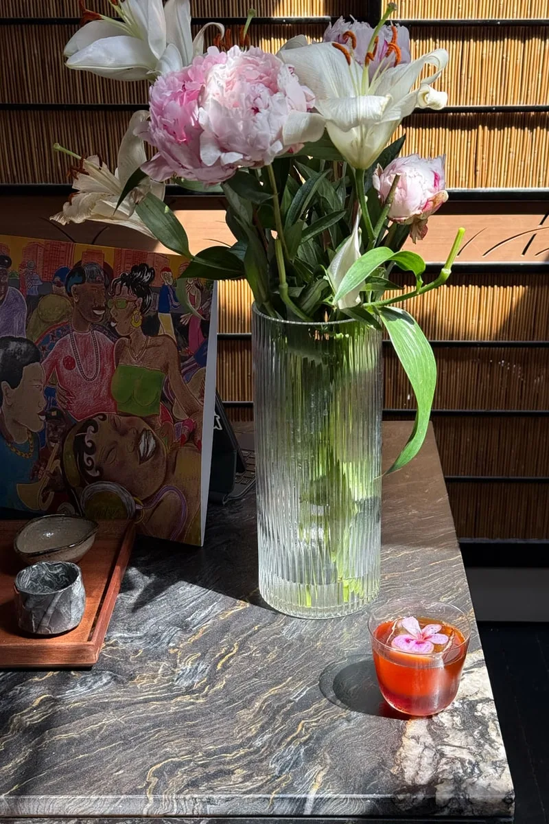 Fleurs dans un vase et boisson sur une table ensoleillée.