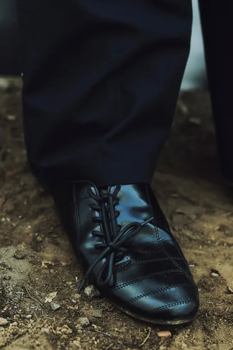 Chaussure noire en cuir avec lacets sur un sol terreux.