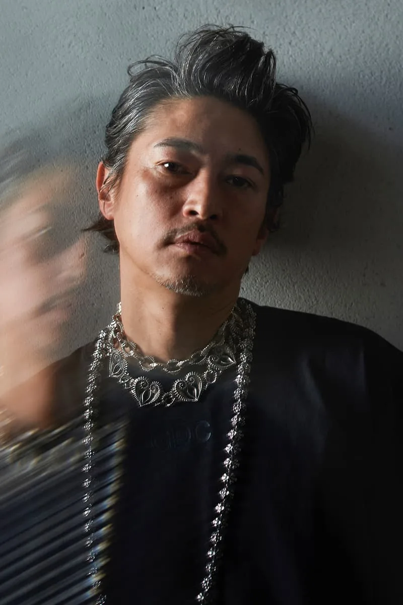 Homme avec chaîne en argent, fond flou, style artistique.