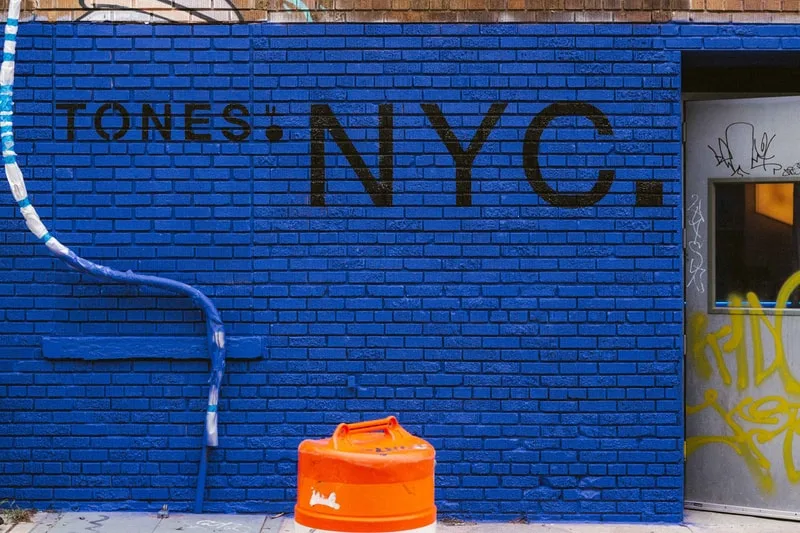 Mur bleu vif avec texte 'TONES. NYC.' et porte graffitée.