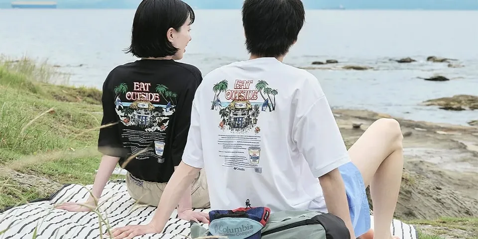 Deux personnes assises près d'un lac avec des t-shirts 'EAT OUTSIDE'.