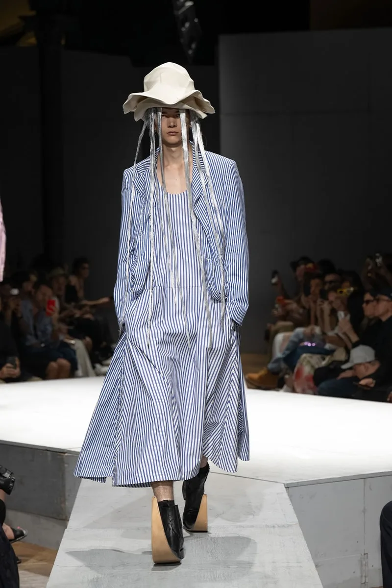 Défilé de mode avec tenue rayée bleue et chapeau excentrique.