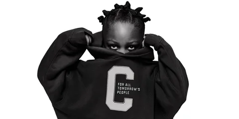 Personne en sweat-shirt noir avec lettre C, se cachant le visage.