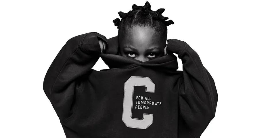 Personne en sweat-shirt noir avec lettre C, se cachant le visage.