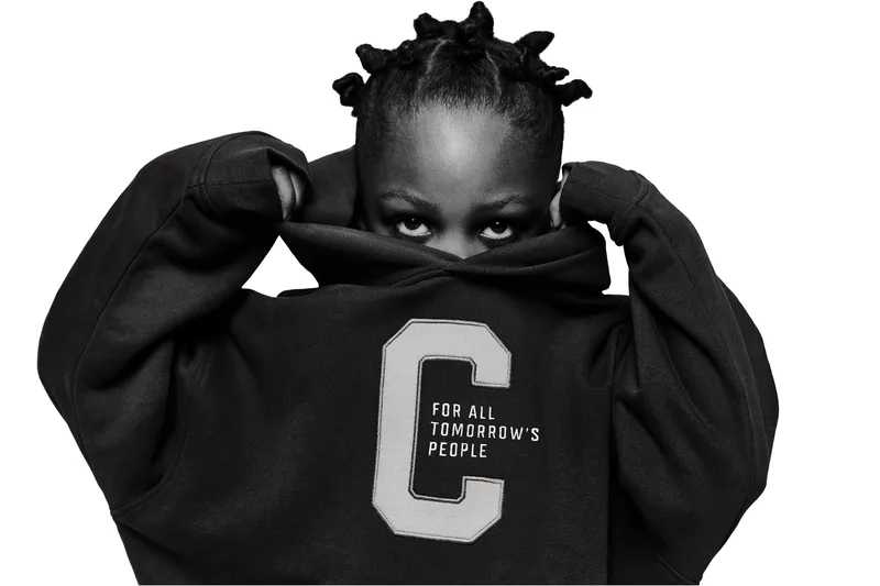 Enfant portant un sweat-shirt avec un C, regarde avec les cheveux en petites tresses.