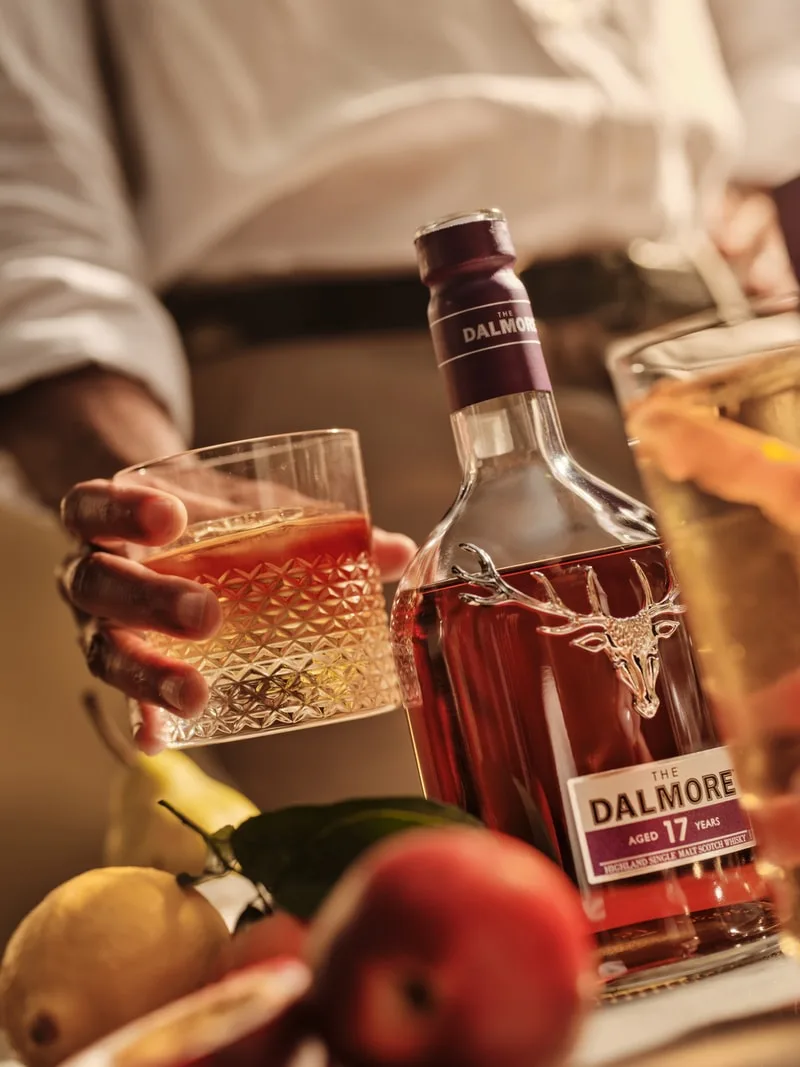 Bouteille de Dalmore 17 ans avec un verre et des fruits sur une table.