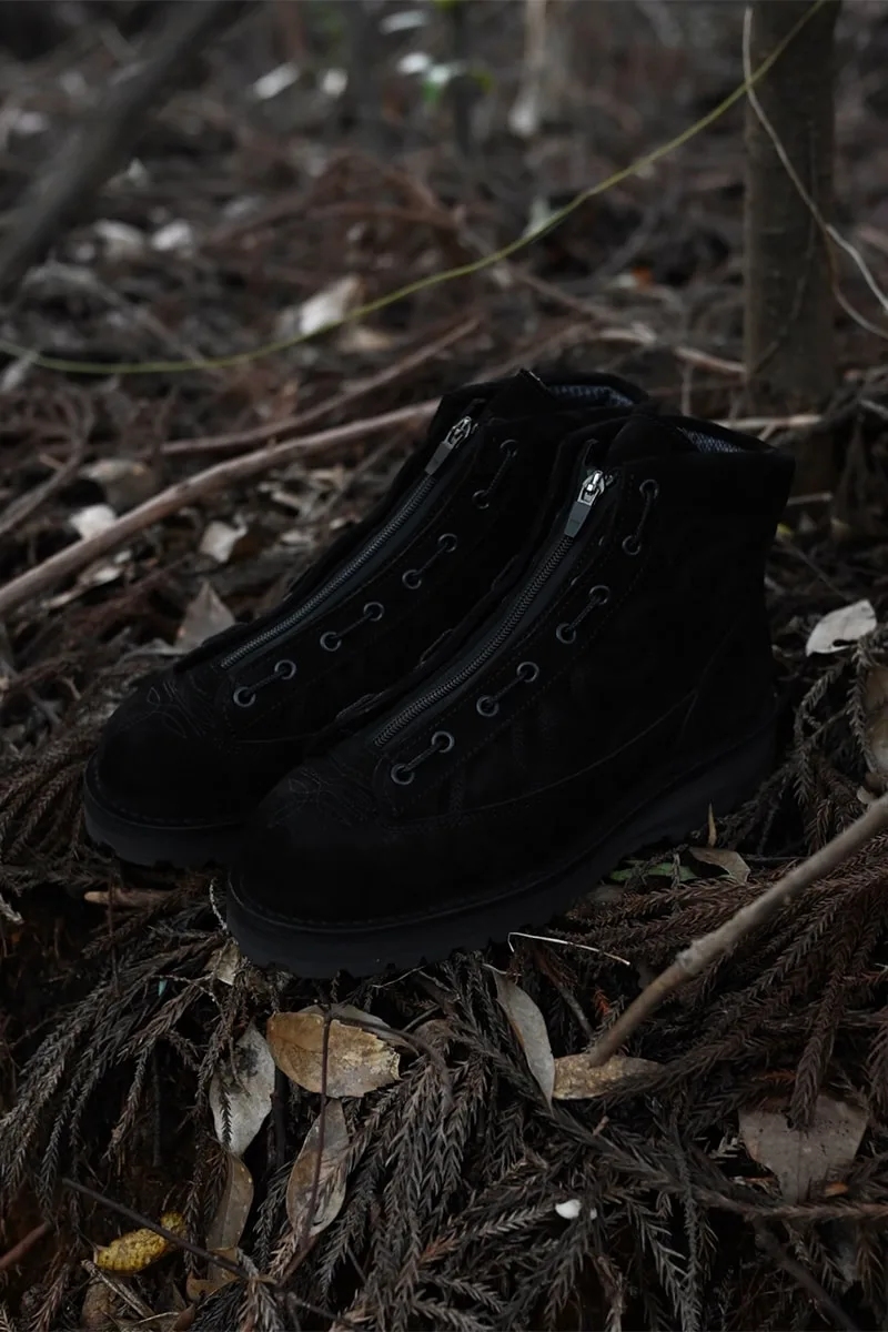 Chaussures noires sur un sol forestier avec des feuilles sèches.