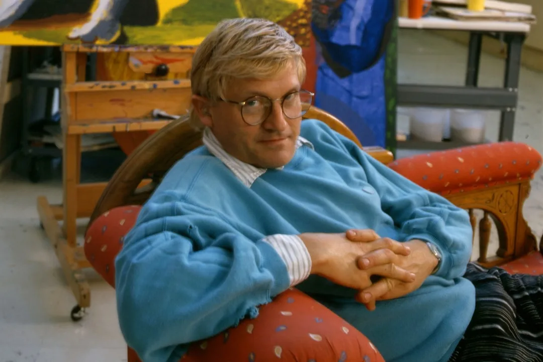 Homme assis avec un pull bleu devant une toile.