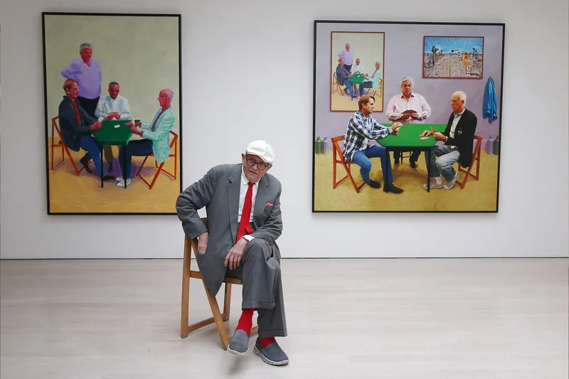 Homme assis devant des tableaux représentant des personnes jouant aux cartes.